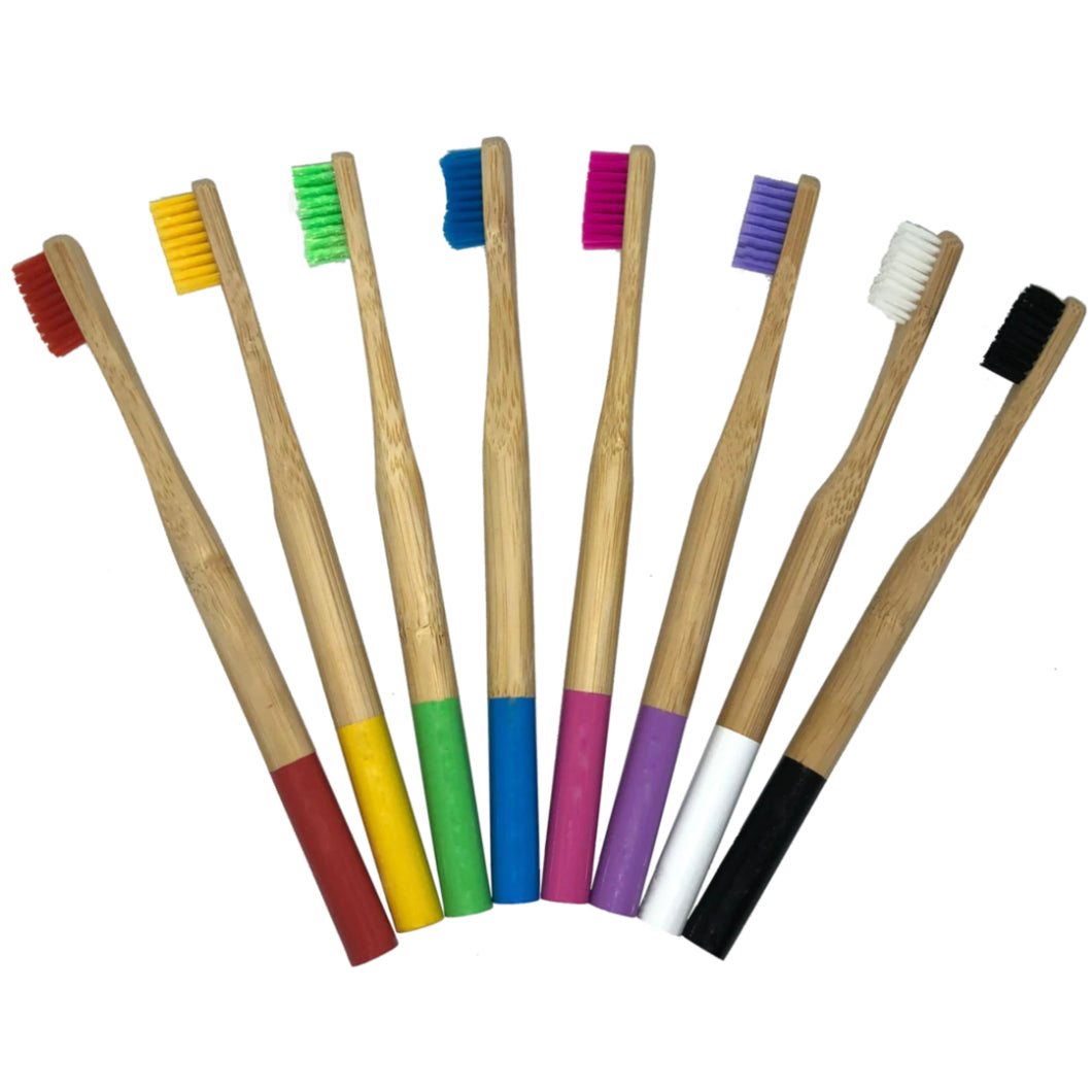 8 bamboo toothbrushes lying on their side. From left to right; red brush with red handle, yellow brush with yellow handle, green brush with green handle, blue brush with blue handle, pink brush with pink handle, purple brush with purple handle, white brush with white handle, black brush with black handle.