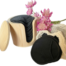 Load image into Gallery viewer, Bamboo cylindrical holder with 17 x black bamboo reusable make up remover pads, with more pads in a mesh laundry bag. Pink flowers adding some colour to the setting. 
